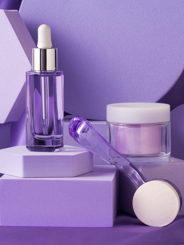 Hyaluronic acid serum bottle and anti aging cream on purple background displayed on geometric shape podiums on silk background